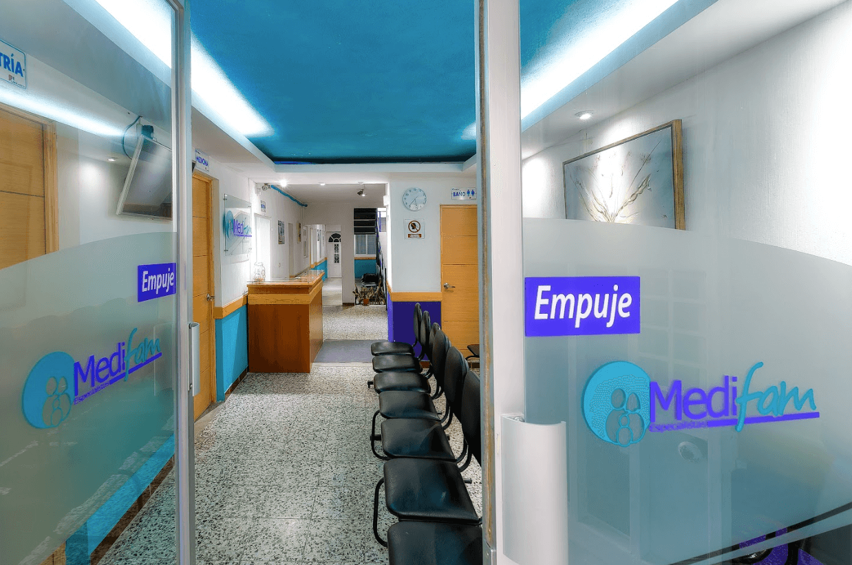 Vista del área de recepción del Hospital Privado MediFam en Sololá, destacando puertas de vidrio con señalización de empuje y logos del centro médico.